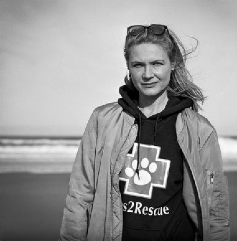 A black and white photo of Paws2Rescue team member Oksana standing on a beach wearing a hoodie with the Paws2Rescue logo printed on the front